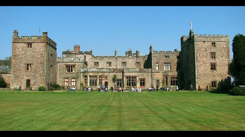 Historic stone castle with two large towers and a central courtyard, set against a clear blue sky with a manicured lawn in front.