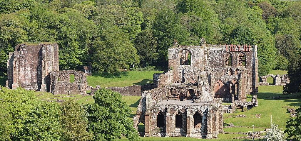 Ruins of a large stone abbey surrounded by lush green trees.