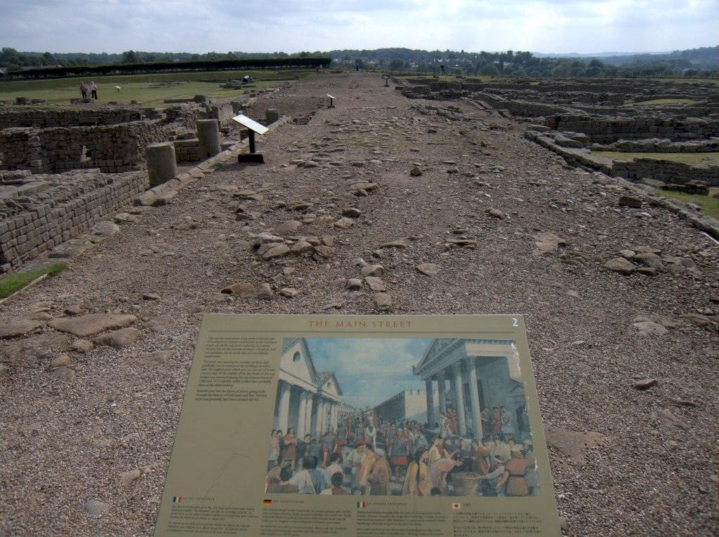 Ancient ruins of a Roman settlement with a sign displaying information and an illustration of what the main street might have looked like in its prime.