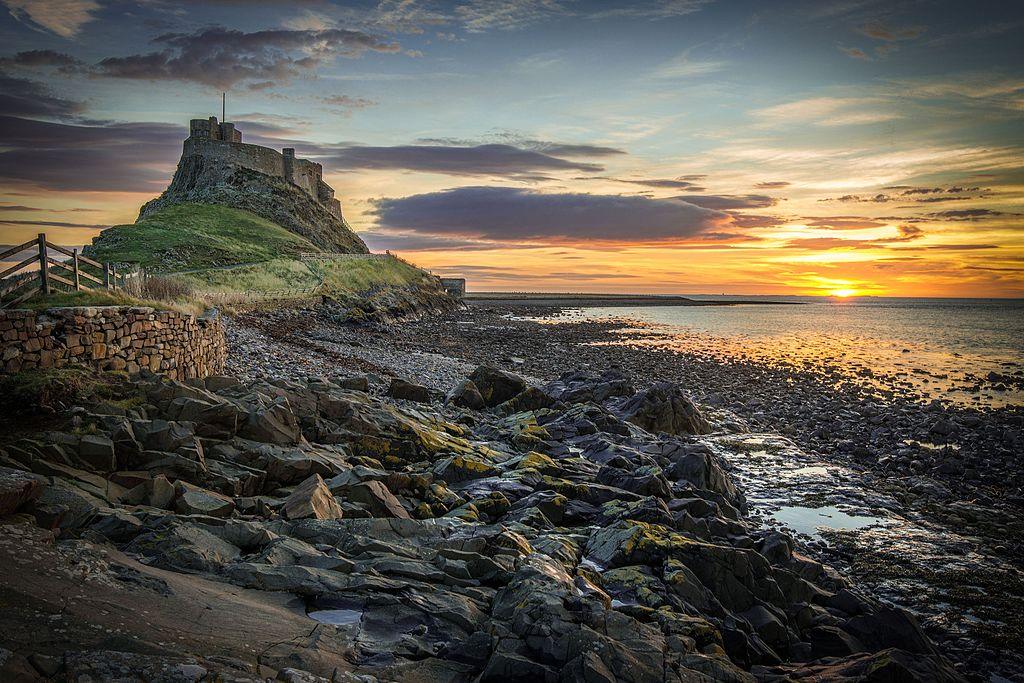 Stone path leading to a castle on a hill by the rocky coastline at sunset.