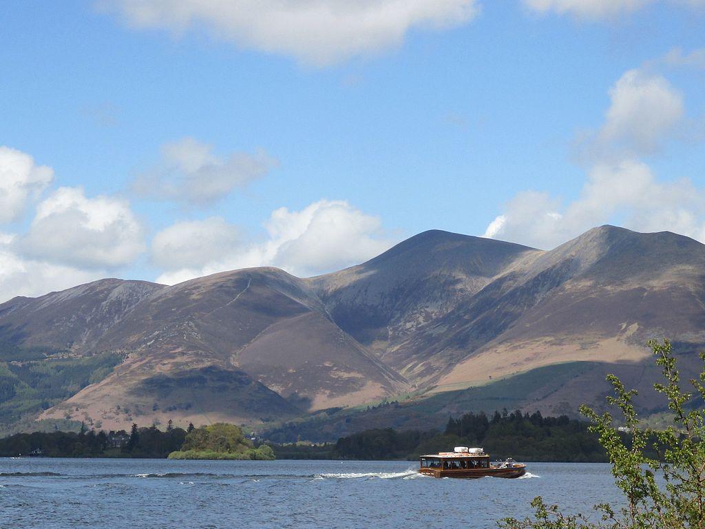 A boat sailing on a lake with large hills in the background under a partly cloudy sky.