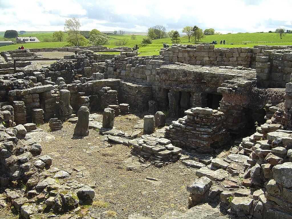 Cumbria | Ruins of a stone building with remnants of walls and columns against a backdrop of grass and trees.