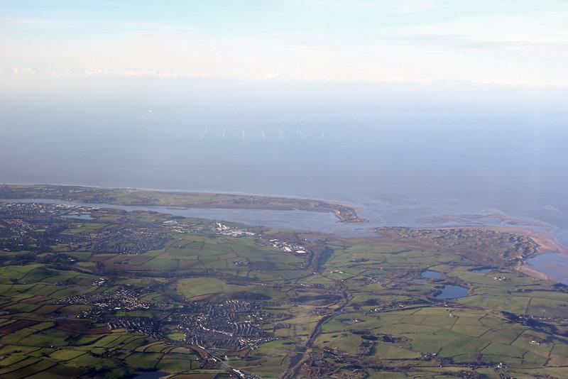 Aerial view of a coastal region with green fields, towns, a river, and the sea extending to the horizon.