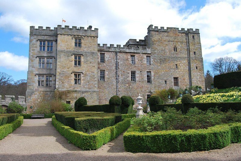 A stone castle with battlements surrounded by manicured gardens and hedges.