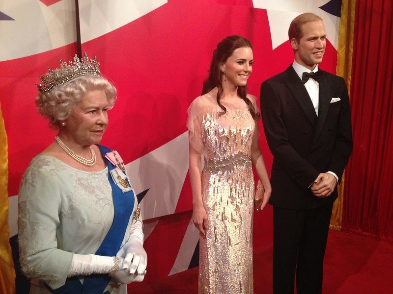 Wax figures of three people in formal attire against a red and white backdrop.