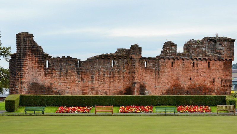 Ancient stone wall with flower beds and benches in the foreground.