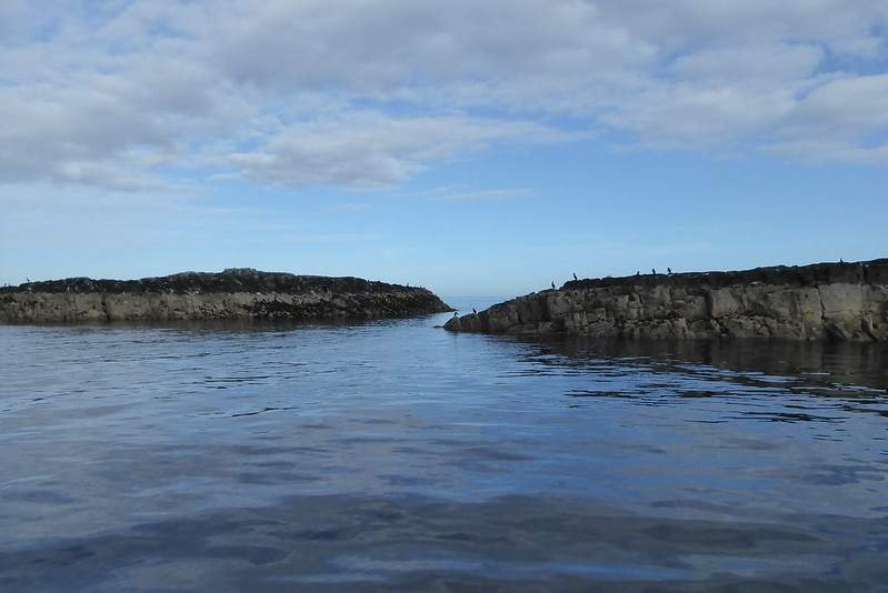 A narrow sea passage between two rocky outcrops under a partly cloudy sky.