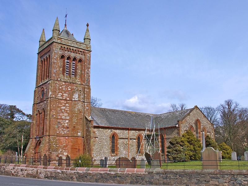 St Michael's Church Bootle | Stone church with a tall, square bell tower, pointed arch windows, and a pitched roof, surrounded by a small graveyard and greenery, under a blue sky.