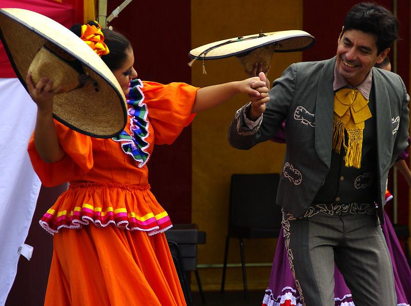 Man and woman in traditional Mexican folk dance attire holding hands and smiling while performing.