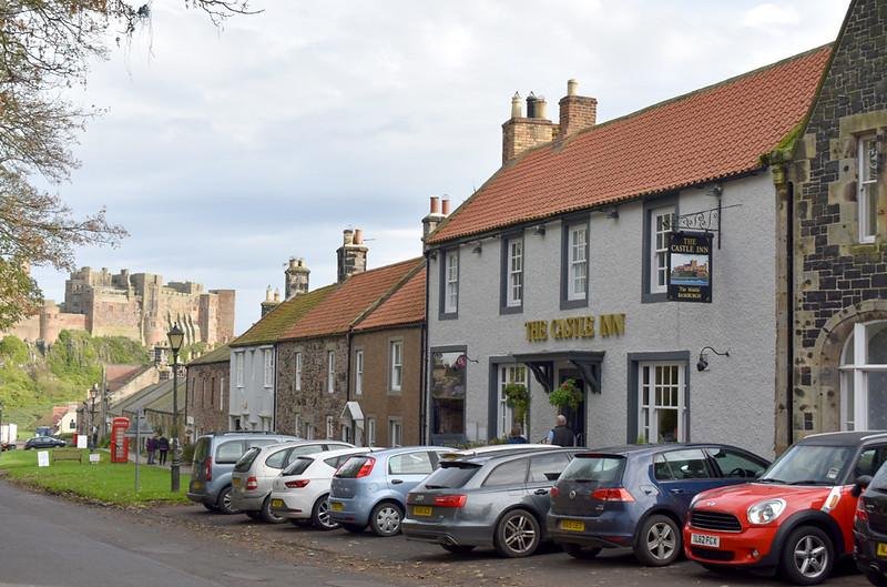 Street view with parked cars, people walking, and a row of buildings including "The Castle Inn"; a castle is visible in the background.