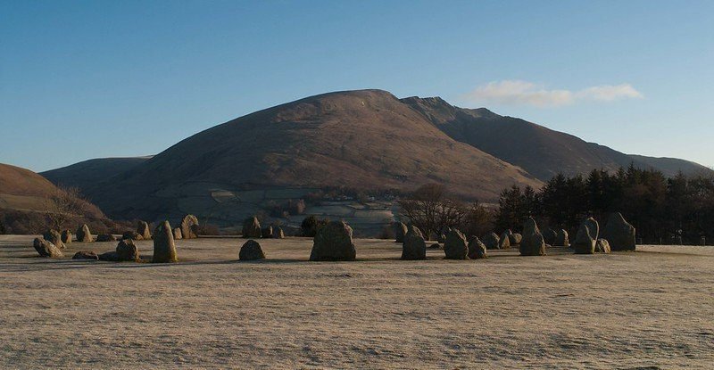 Stone circle on a frosty field with a mountain in the background, under a clear blue sky.