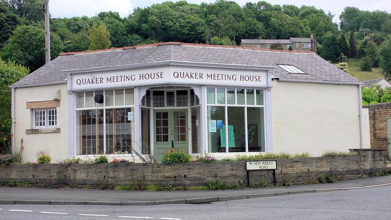 Quaker Meeting House building with large windows and a sign indicating its name, located on New Ridley Road, surrounded by greenery.