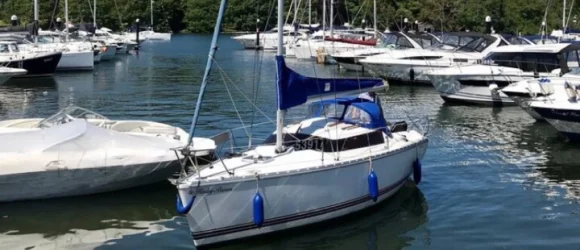 A docked sailing boat with blue fenders and a blue canopy, surrounded by other boats on a calm water marina.