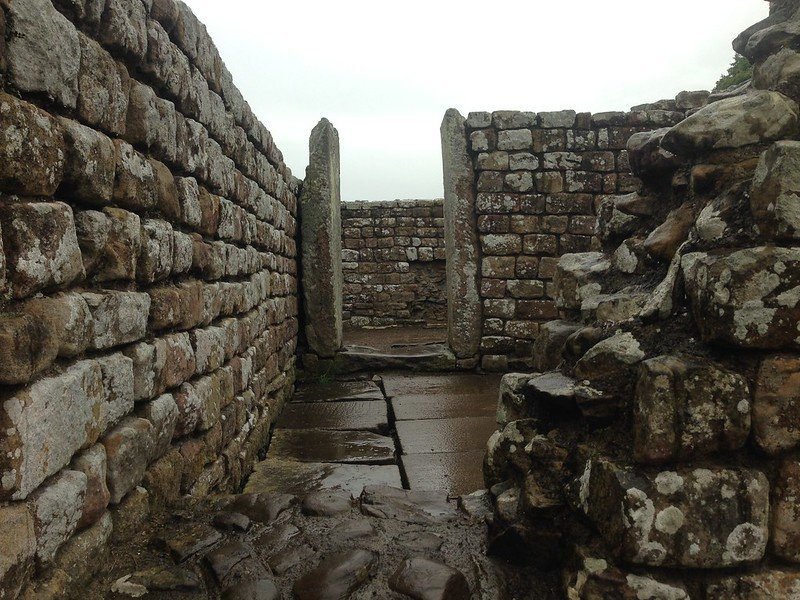 Stone walls and pathway of a historic structure, with upright stones flanking the entrance.