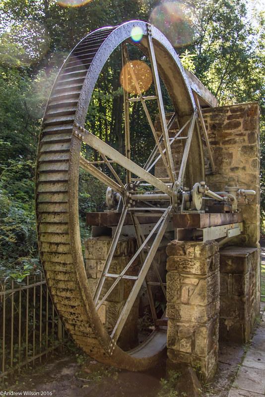 Cragside | The World’s First Electrically Lit Home | Old watermill wheel in a wooded area with sunlight filtering through trees.