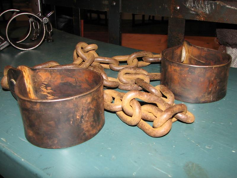 Rusty metal shackles with attached chains on a teal surface.