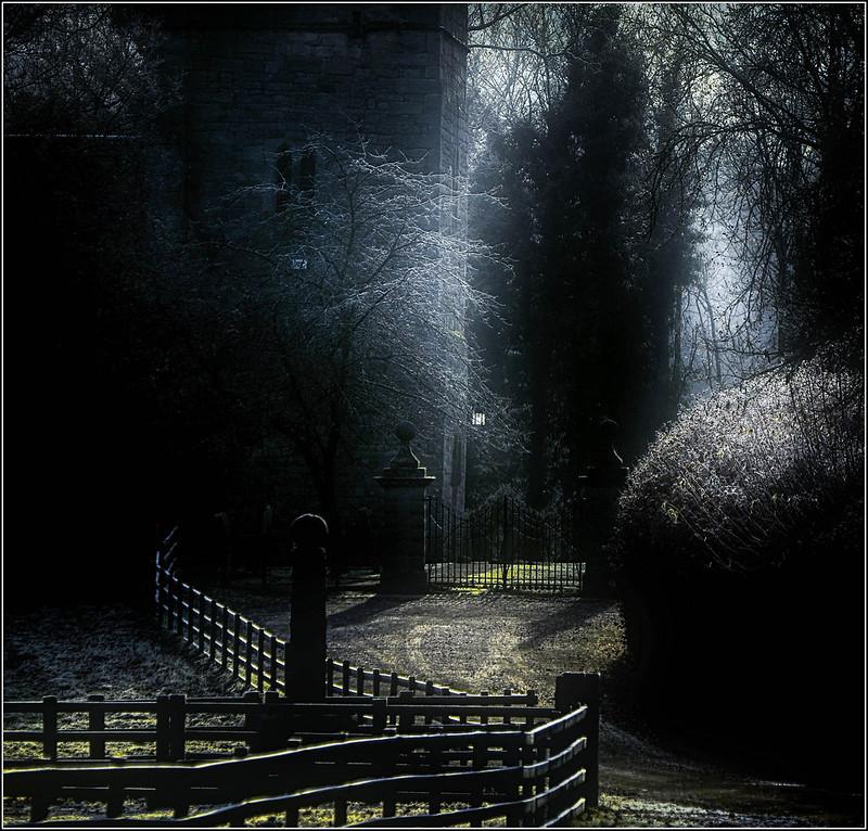 Pathway leading to an old iron gate surrounded by frosty trees and wooden fences, illuminated by soft morning light.