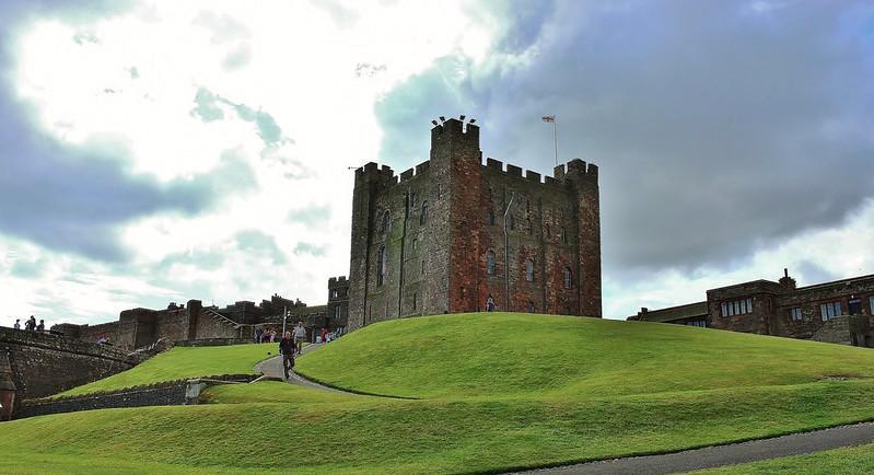 Medieval castle on a hill with green lawns and a cloudy sky in the background.