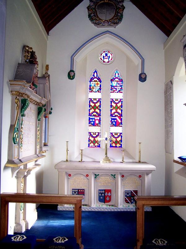 Aspatria | Small chapel interior with stained glass windows, an ornate altar, and memorial plaques on the walls.