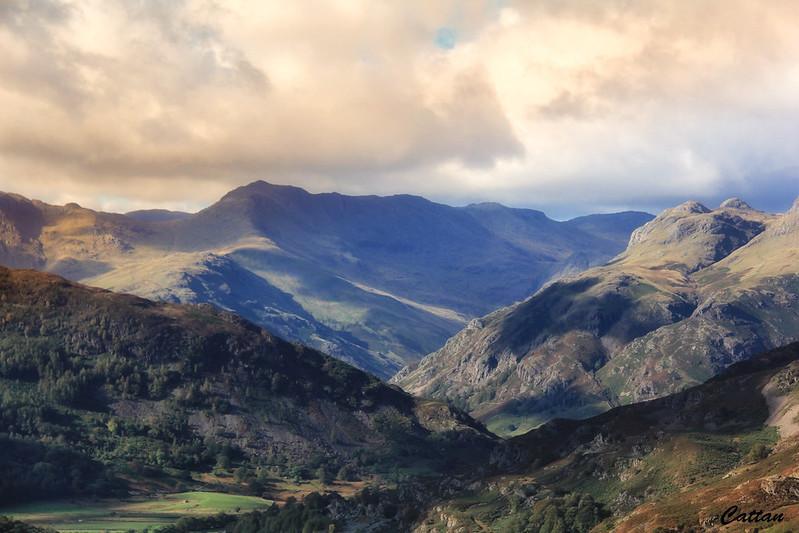 Scafell Pike, Lake District, Cumbria | Misty mountain landscape with lush green slopes and rugged peaks under a partly cloudy sky.