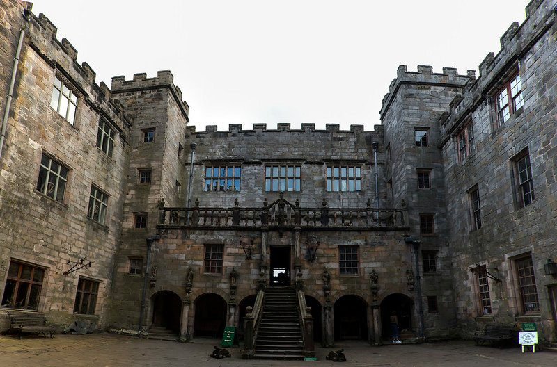 Stone courtyard of an old castle with crenellated towers and arched entryways.