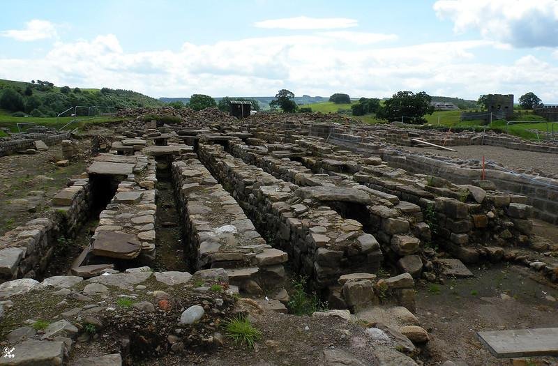 Ruins of ancient stone structures on a grassy hillside under a cloudy sky.