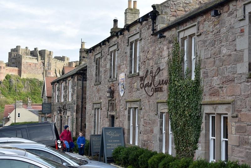 Stone building with a sign reading "Lords Crewe," with a castle visible in the background and parked cars in front.