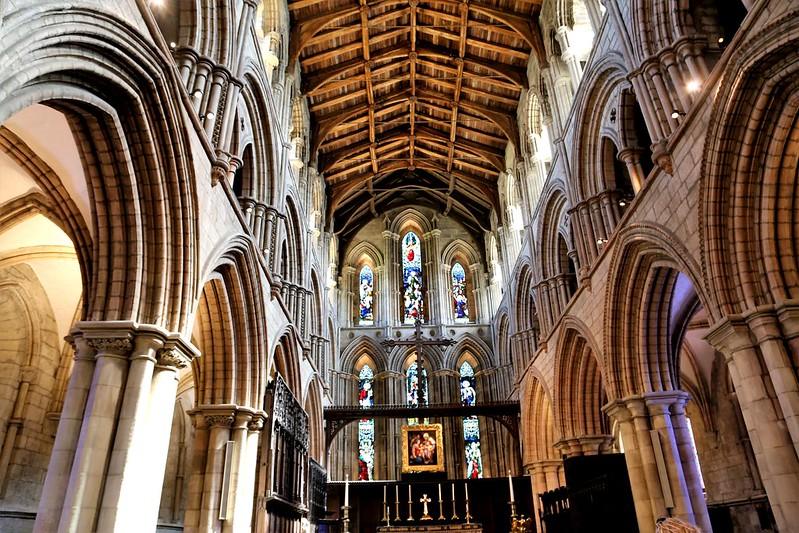 Interior of a Gothic-style cathedral with high arches, stained glass windows, and a wooden ceiling.