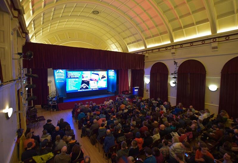 Kendal Mountain Festival, Cumbria | Audience seated in a theatre with a large screen displaying 'Kendal Mountain Festival' and 'Children’s Literature at Kendal'.