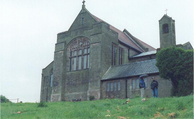 St. Mary's Church, Barrow-in-Furness, England | Stone church building with large arched windows and a bell tower, surrounded by green grass, with two people standing near the entrance.