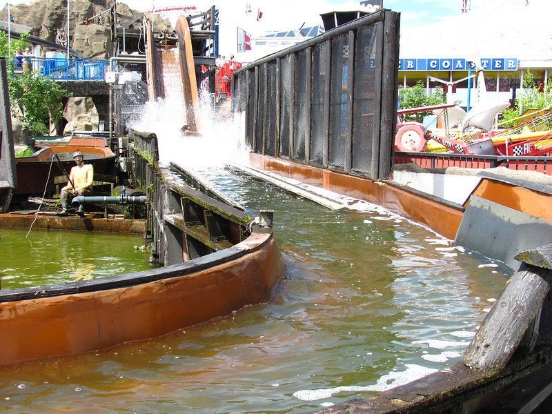 Log flume ride with boat descending water slide into splash pool at amusement park.