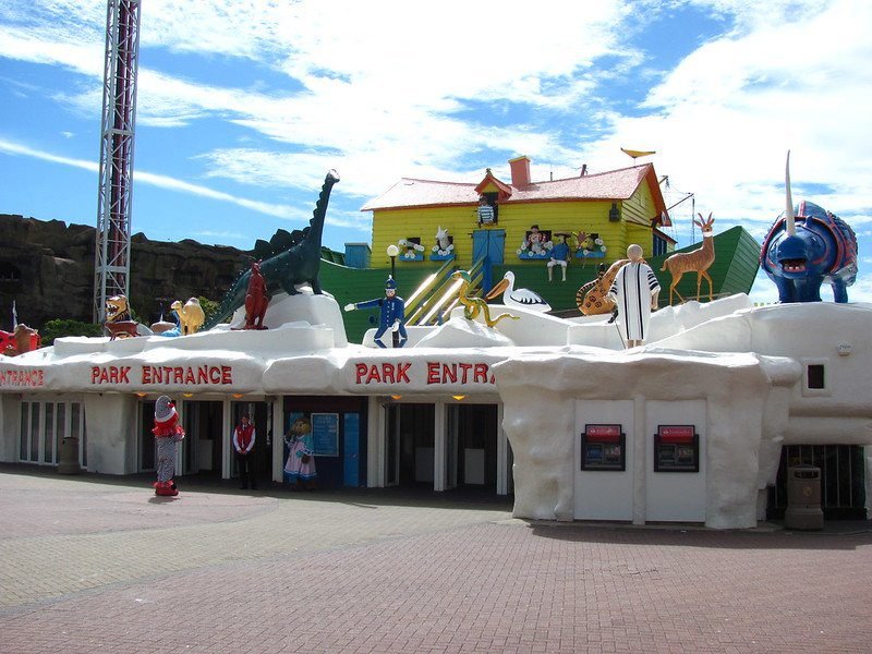 Theme park entrance with colourful, whimsical animal and character sculptures on a snow-like structure, featuring a house and various figures like a dinosaur and police officer.