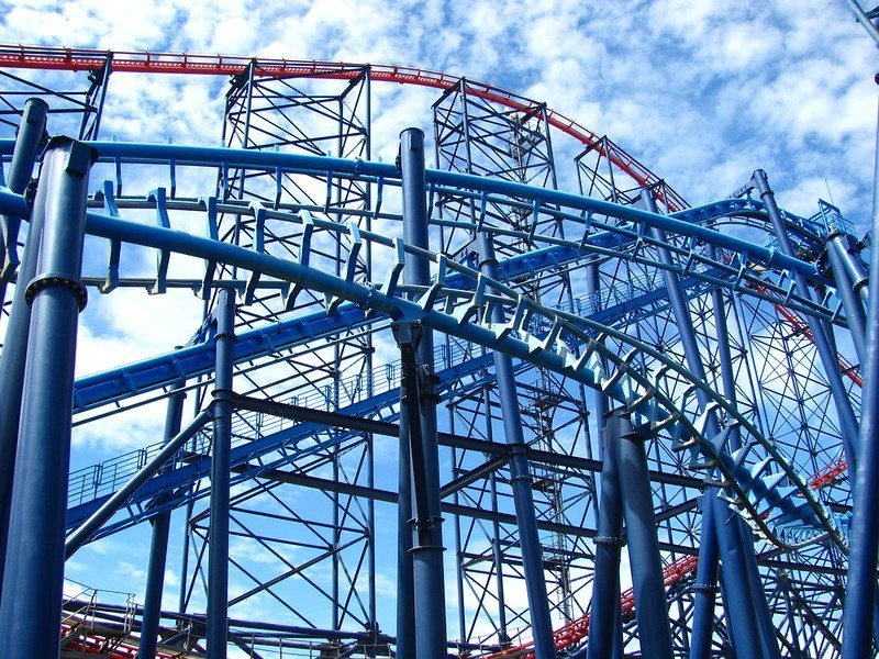 Blue and red steel roller coaster track under a partly cloudy sky.