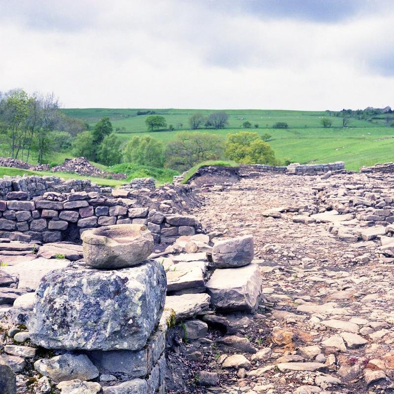 An ancient stone ruin in a green, grassy landscape under a cloudy sky.