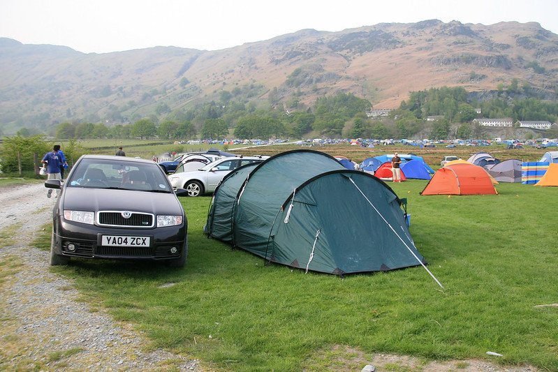 Car parked next to a green tent on a camping site with hills in the background.