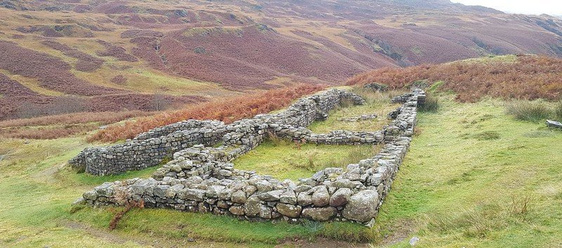 Ruins of an ancient stone structure surrounded by grassy and hilly terrain.