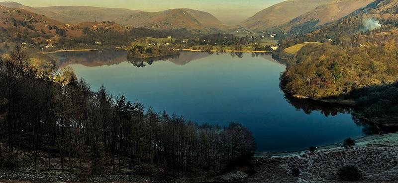 A serene lake surrounded by rolling hills and dense trees, with a clear reflection of the landscape on the water's surface.