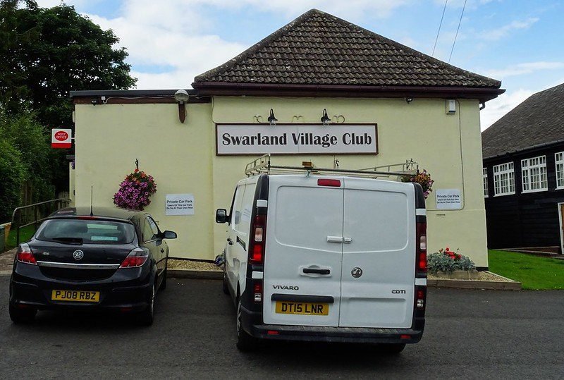 White van and black car parked in front of Swarland Village Club building.