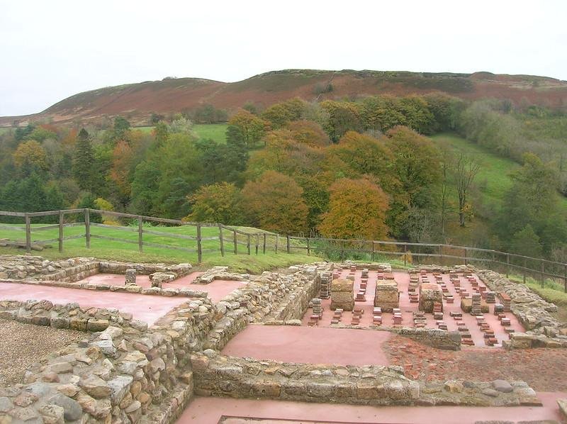 Ancient Roman ruins with a scenic view of green and autumnal forested hills in the background.