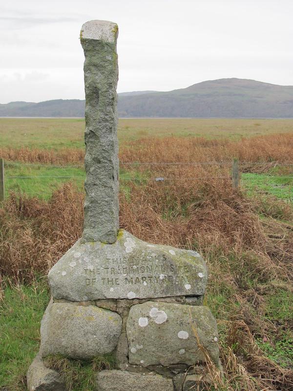 Wigton | Stone monument inscribed with "This marks the traditional site of the martyrdom," set in a grassy field with hills in the background.