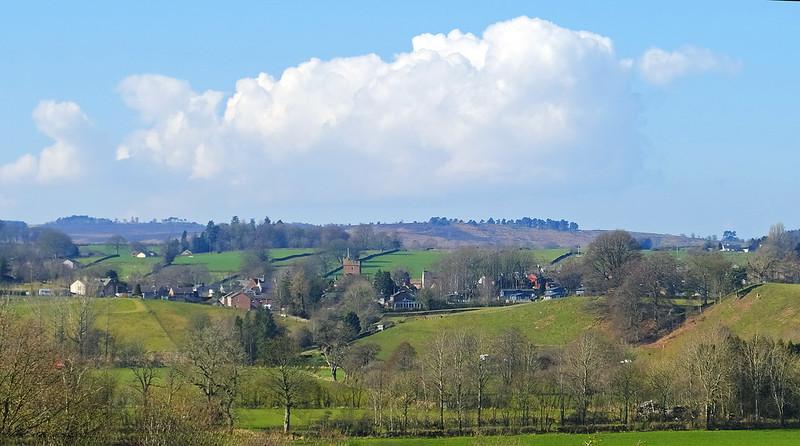 Great Salkeld | Rolling countryside with green fields, scattered houses, and trees under a clear blue sky with large white clouds in the background.