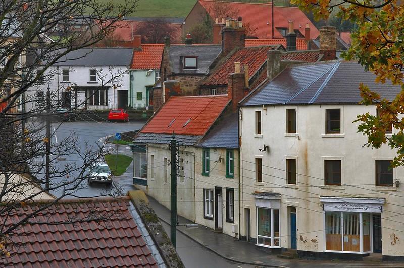 A view of a small town with old buildings, red-tiled roofs, and narrow streets on a rainy day.