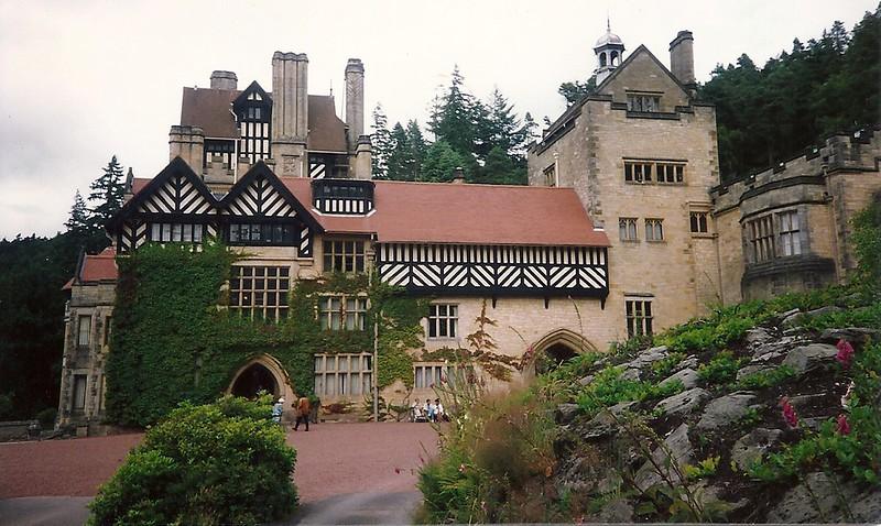 Large historic building with half-timbered sections and ivy-covered walls, surrounded by trees and a gravel courtyard.