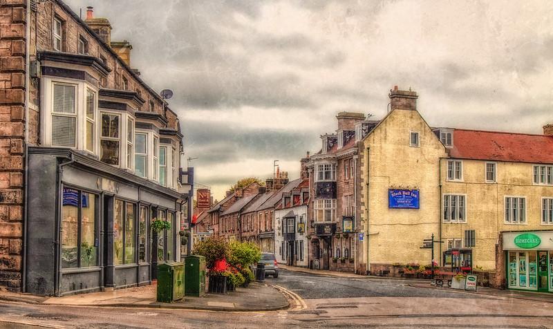 A picturesque street in a small town with historic buildings, shops, and a moody sky.