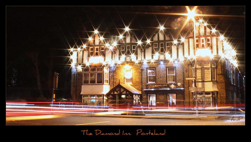 The Diamond Inn at night, brightly lit with starburst effects from lights, cars passing in front leaving light trails.