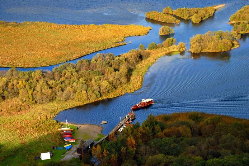 Aerial view of a boat approaching a dock surrounded by lush greenery and waterways, with additional small islands visible in the background.