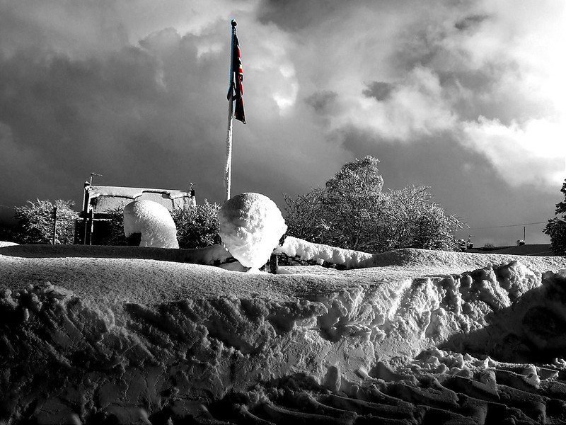 Snow-covered landscape with a colourful flag in the background and dramatic cloudy sky.