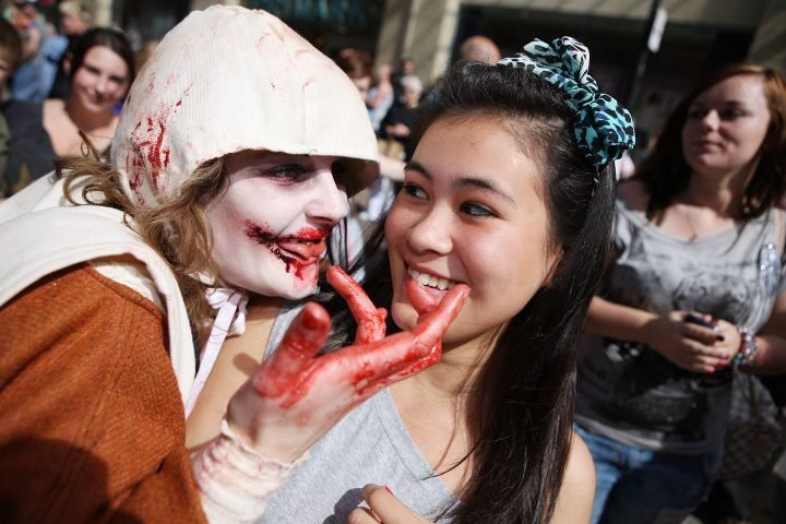 A person in zombie makeup playfully interacts with a smiling girl in a crowd.