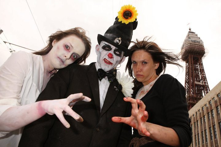 Three people in zombie makeup and costumes posing in front of a tower.