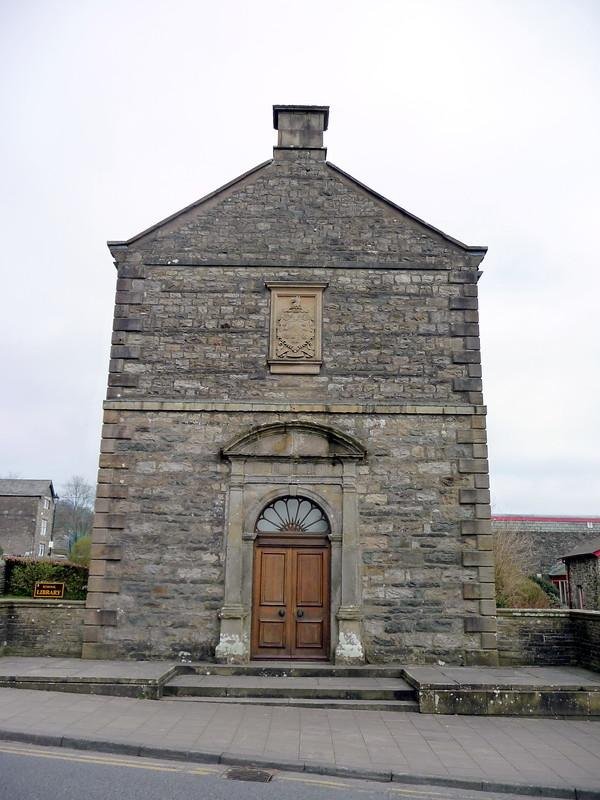 Sedbergh library | Stone building with a gabled roof, arched wooden door, and a coat of arms above the entrance.